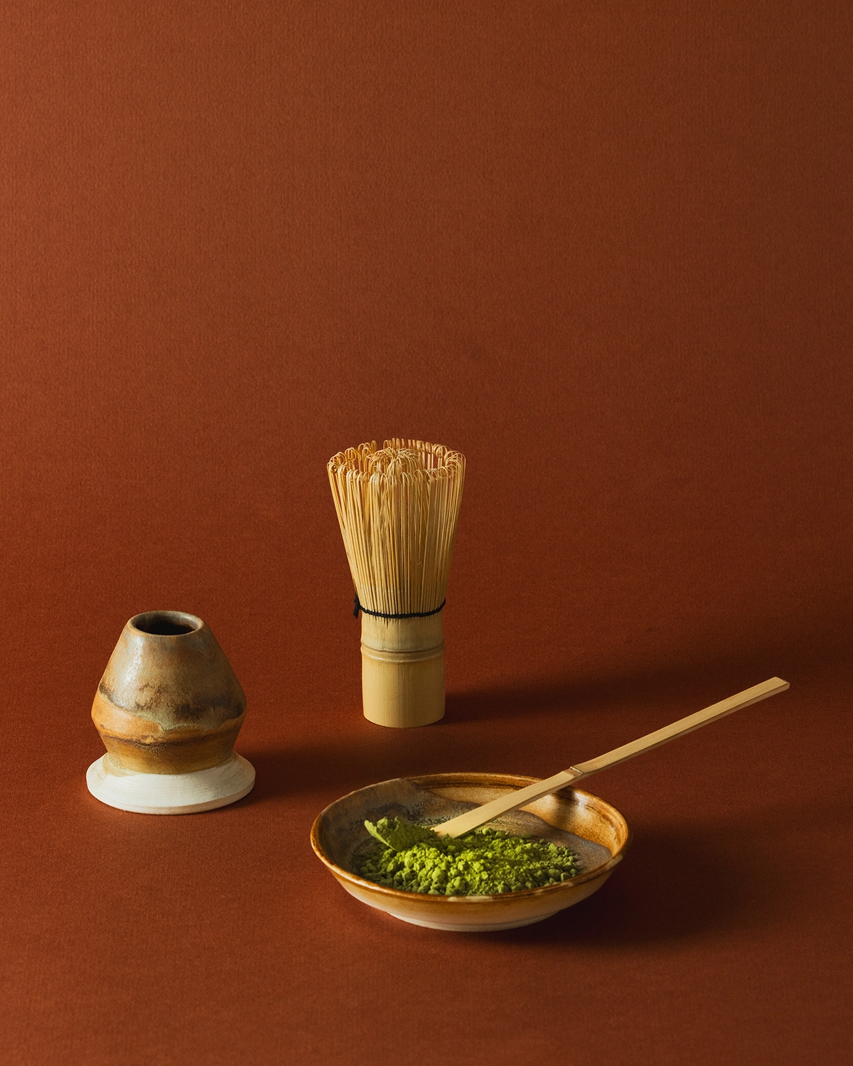 Matcha en polvo, batidor chasen y cuenco de cerámica sobre fondo terracota